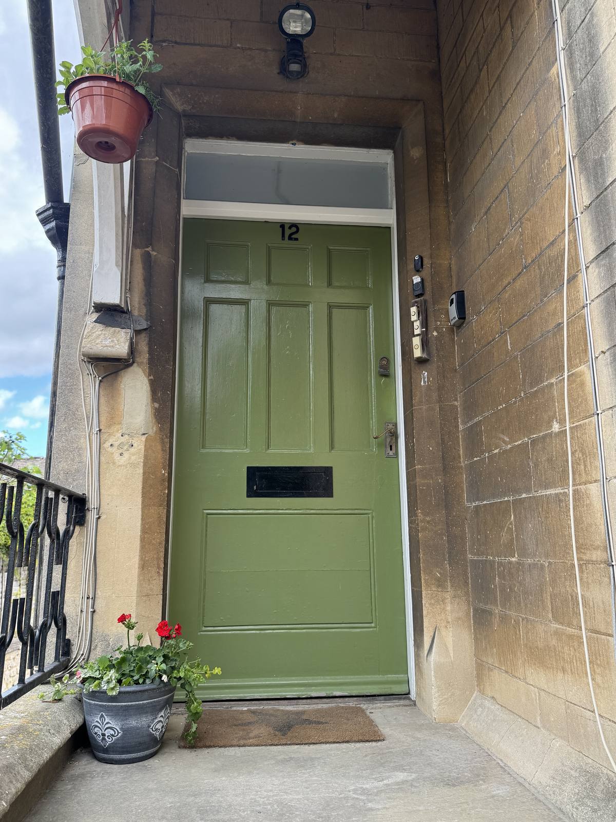 Green front door of the building at number 12, with potted geraniums