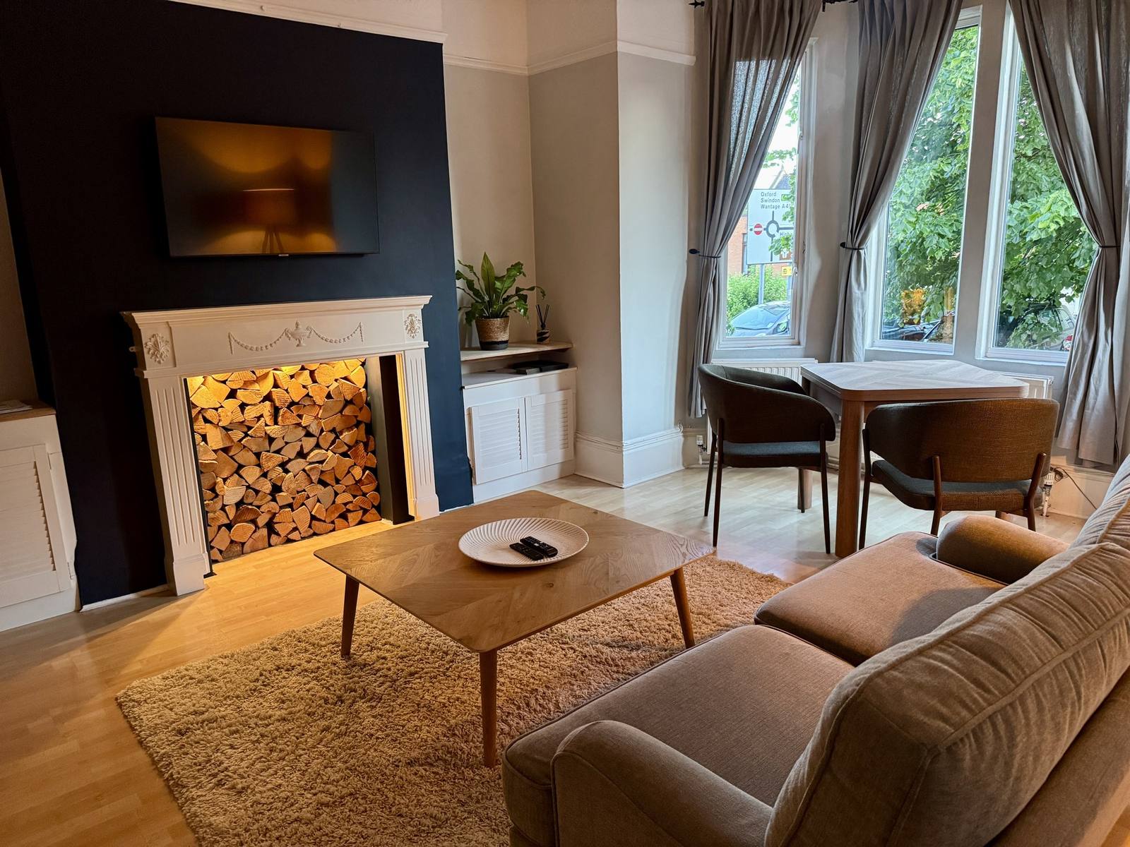 Bright living room at The Faringdon Flat with a feature fireplace, comfortable sofa and a dining table beside the bay window